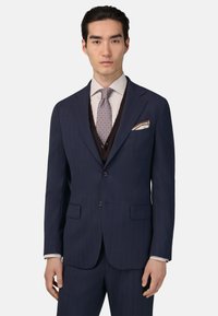 Tumes sinelõngadega ülikond, millel on sakiline krae, kahe nupuga kinnitamine ja topelt tagumine lõhik. Kombineeritud heledate triipudega pluusiga ja mustrilise lipsuga.