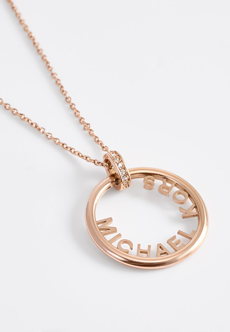 Collier pendentif en or rose présentant un design circulaire avec des lettres découpées épelant "MICHAEL KORS", accentué d'un petit strass.