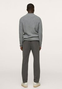 Grau gerippter Pullover kombiniert mit grauen Sweatpants, getragen mit weißen und beigen Sneakers. Weiche Textur, lockere Passform, minimalistisches Design.