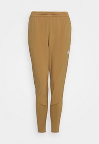 Bruna träningsbyxor med en figurnära design, tillverkade av ett glatt material. Har en mesh-midja och en subtil varumärkeslogga på sidan.