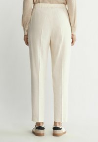 Ljust beige byxor med en smal passform, som har en slät textur, elastisk midja och centrala veck, i kombination med avslappnade skor.