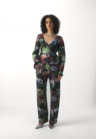 Ensemble à motifs floraux comprenant un haut croisé avec un décolleté en V et un pantalon palazzo en couleurs vives sur fond noir ; talons métalliques.
