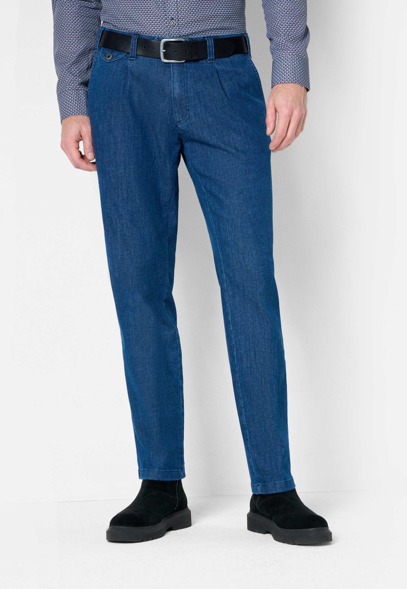 Pantalons en denim bleu foncé à coupe droite, avec une ceinture à boucle noire, portés avec des bottines noires.