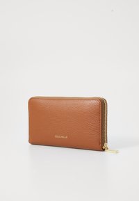 Portefeuille Coccinelle en cuir brun texturé, forme rectangulaire, fermeture éclair dorée et logo embossé sur le devant. Comprend un anneau de tirage sur la fermeture éclair.