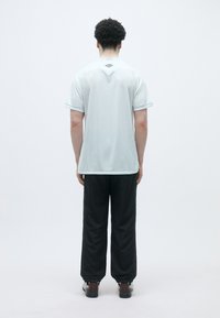 Gaiši zils sporta krekls ar īsām piedurknēm, ar apaļu kakla izgriezumu un diskrētām akcentiem pie piedurknēm. Valkāts kopā ar melniem sporta biksēm.