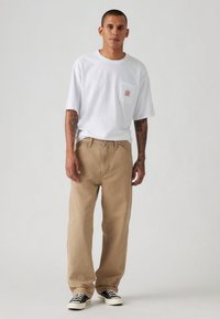 Bela majica s kratkimi rokavi in žepnim detajlom, kombinirana s širokimi bež hlačami in črnimi supergami. Gladek bombažni material.