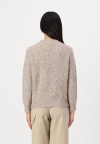 Beige kötött pulóver laza szabással, bordázott textúrával, kerek nyakkivágással és hosszú ujjal. Beig színű cargo nadrággal párosítva, hátulról nézve.