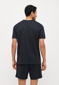 T-shirt en coton noir à manches courtes, coupe décontractée et décolleté ras du cou, associé à un short noir assorti pour un look coordonné.