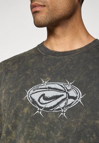Mørkegrøn tie-dye bomulds t-shirt med et fremtrædende hvidt Nike-logo omgivet af et pigget design på forsiden. Rund halsudskæring.
