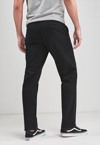 Schwarze Baumwollhosen mit geradem Schnitt, seitlichen und hinteren Taschen, glatter Textur und leichtem Glanz. Kombiniert mit schwarz-weißen Sneakers.