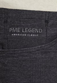 Tmavě šedá látka se jemným kostkovaným vzorem. Na zadní kapse je vyšitý nápis "PME LEGEND" a "AMERICAN CLASSIC" ve světle šedé barvě.