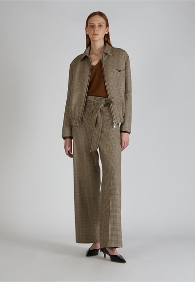 Bruin geruite cropped jas en bijpassende wijde broek, gedragen met een bruine top en zwarte hakken. Subtiele texturen en patronen zichtbaar.