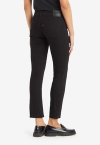 Fekete, slim fit farmernadrág, texturált felülettel, hátsó zsebekkel. Fekete mokaszinokkal viselve.