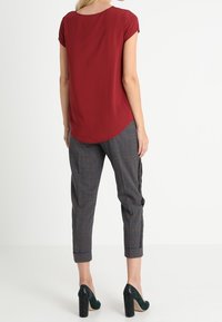 Top rojo de mangas cortas con dobladillo redondeado, combinado con pantalones de cuadros grises de corte ajustado y con puños enrollados. Zapatos de tacón altos negros.