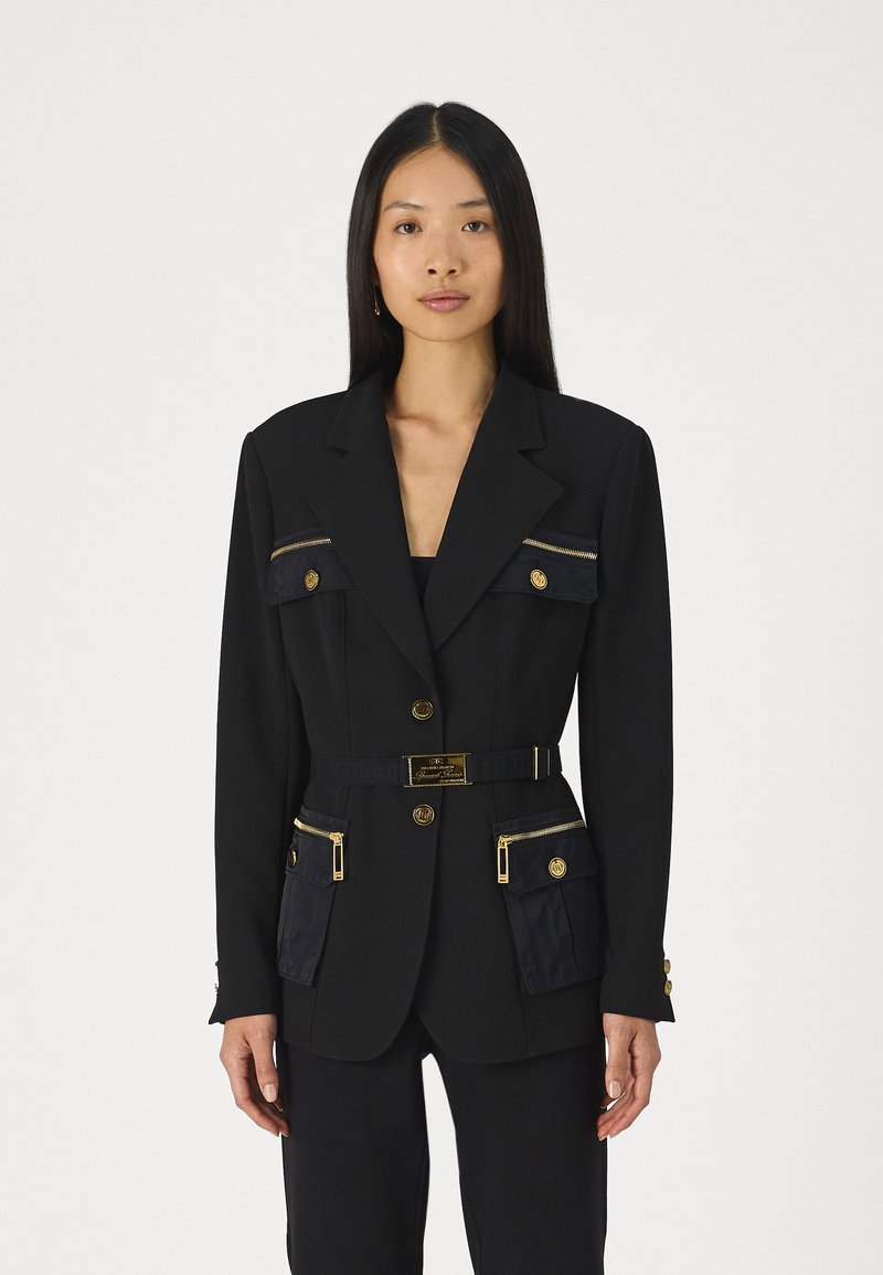 Blazer noir avec boutons dorés, poches zippées et une ceinture avec logo. Coupe ajustée avec manches longues et textures de tissu contrastantes.