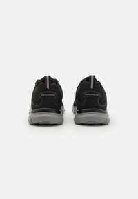 Crne atletske tenisice s mrežastim gornjim dijelom, udobnom sivom potplatom i trakom za povlačenje na peti s logotipom "SKECHERS".