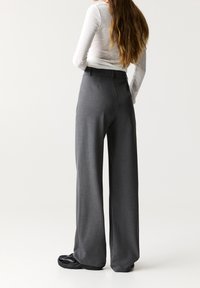 Pantalons larges gris en tissu texturé, dotés d'une taille haute et d'une finition soignée, accompagnés de chaussures noires.