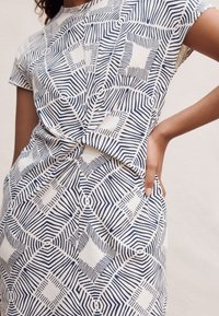 Katoenen jurk met een geometrisch patroon in blauw en wit. Korte mouwen, losse pasvorm, met een knoopdetail in de taille.
