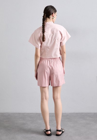 Lichtroze katoenen shirt met korte mouwen, gecombineerd met lichtroze gestreepte shorts. De achterkant heeft een elastische tailleband en een enkele achterzak.