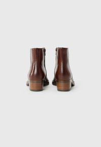 Bottines en cuir marron avec une finition lisse, fermeture éclair et un talon en bois empilé. Le design présente des bords arrondis et épurés.