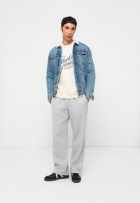 Jeansjacka med en fleecekrage, vit grafisk sweatshirt, grå sweatpants och svarta sneakers med vita detaljer. Avslappnad passform.