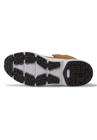 Zapatilla de ante marrón con una suela de goma blanca. Presenta una suela exterior texturizada negra con acentos rojos y un distintivo logo de DC.