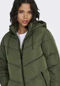 Green puffer jacket with a hood, featuring a zippered front, side pockets, and a quilted design. Made from a smooth, water-resistant fabric.