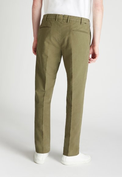 Pantalones verde oliva claros con un corte recto, que presentan bolsillos traseros y una tela suave, ligeramente texturizada. Llevados con zapatillas blancas.