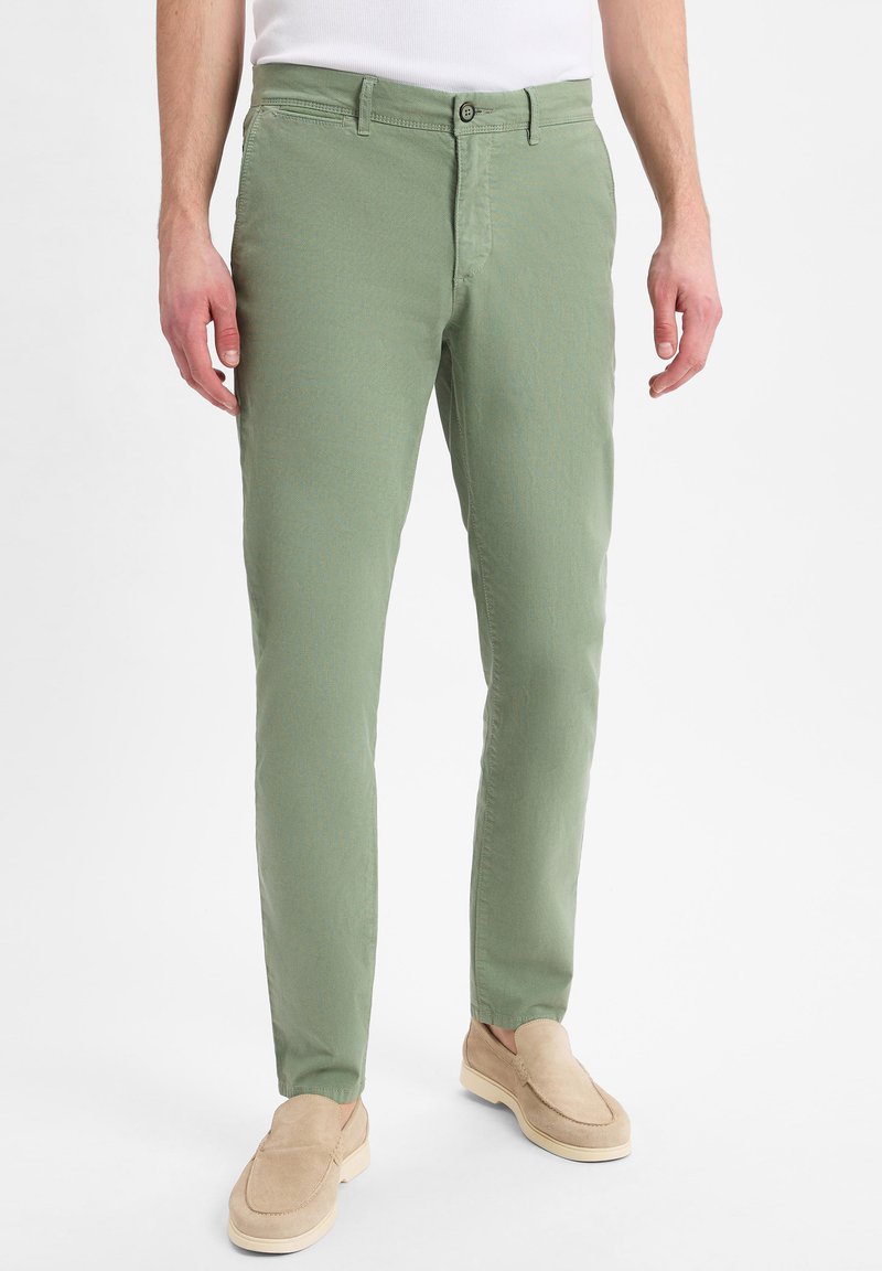 Hellgrüne Baumwollchinos mit Slim-Fit, ausgestattet mit einem Reißverschluss, Knopfverschluss und Fronttaschen. Tragen mit beigen Slippers.