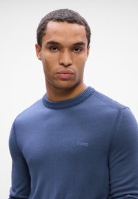 Crewneck sweater in dark blue, knit fabric. Features subtle "BOSS" logo embroidered on chest. Classic fit with ribbed collar and cuffs.