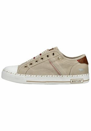Beige lage canvas sneaker met witte rubberen zool en neuskap, metalen oogjes en een bruine hieltab, met het label "Mustang" op de zool.