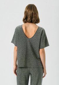Bluza scurtă cu mâneci, lejeră, dintr-un material gri metalic, cu un decolteu adânc la spate. Textura pare netedă, cu o strălucire subtilă.