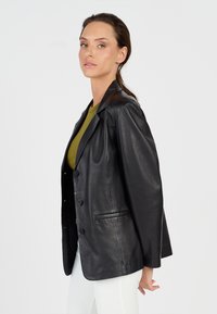 Zwarte leren blazer met een relaxte pasvorm, voorzien van een geknipt kraag, vier knopen en zijzakken. Soepele textuur, minimale glans.