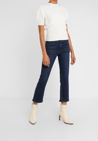 Top blanco de manga corta acanalado, jeans azul oscuro de pierna recta y botas de tobillo cremosas con tacón. Las botas tienen un cierre lateral de cremallera.
