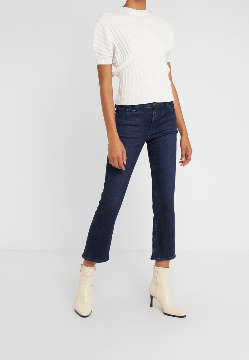 Top blanco de manga corta acanalado, jeans azul oscuro de pierna recta y botas de tobillo cremosas con tacón. Las botas tienen un cierre lateral de cremallera.