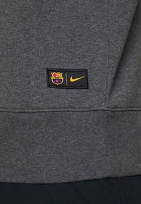 Logos du FC Barcelone et de Nike jaune sur un écusson noir cousu sur un vêtement en tissu gris foncé.