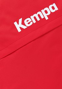 Rode stof met een gestructureerd oppervlak en een prominent wit 'Kempa'-logo, weergegeven in een schone, vetgedrukte typografie.