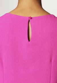 Fuchsiablus med en mjuk textur, med ett nyckelhålsdetalj bak och en knappstängning högst upp.