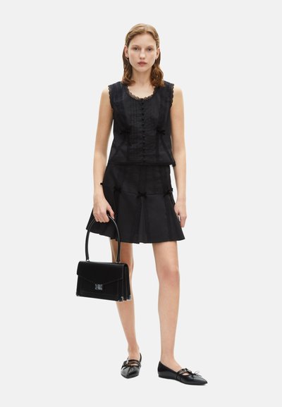 Top in pizzo e tessuto nero con bottoni, abbinato a una gonna nera svasata. Gli accessori includono una borsa nera e scarpe basse con fiocchi.