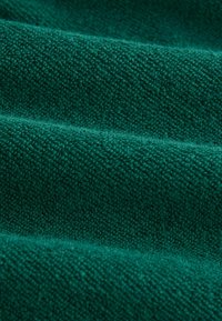 Teal tekstureret stof med en tæt vævning, hvor synlige forhøjede fibre skaber en blød, taktil overflade, arrangeret i bløde folder.