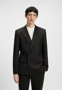 Schwarzer doppelt knöpfbarer Blazer mit Spitzrevers, zwei vorderen Taschen und schwarzen Knöpfen, kombiniert mit einem weißen Rundhals-T-Shirt. Glatte Textur.