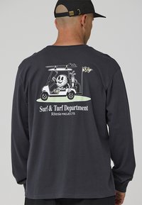Camiseta de manga larga de algodón gris oscuro, con un gráfico de dibujos animados de un carrito de golf en la parte trasera acompañado del texto "Departamento de Surf y Turf".
