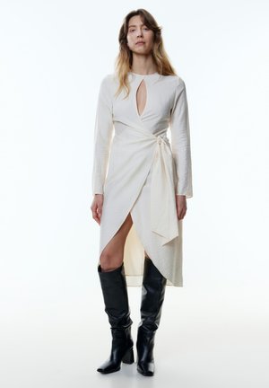Langarm, crème wrap jurk met een sleutelgat halslijn en zijriemdetail; gecombineerd met kniehoge zwarte leren laarzen, met vierkante neus.