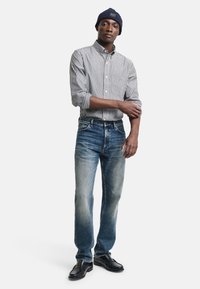 Gestreepte blouse met lange mouwen in wit en marineblauw, gecombineerd met vervaagde blauwe rechte jeans en zwarte leren schoenen.