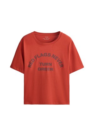 T-shirt rouge à manches courtes avec col rond et texte noir indiquant "RED FLAGS NEVER TURN GREEN" sur le devant.