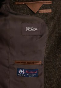 Motivo a zigzag in tessuto tweed marrone e verde; presenta una fodera in satin marrone, etichette delle tasche con "Oscar Jacobson" e "Moon Shetland."