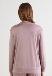 Suéter de manga larga en suave tela lavanda, con cuello redondo, puños ajustados y un detalle de costura horizontal en la parte trasera.