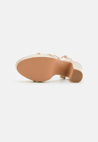 Sandal con tacco con tomaia in oro metallico, texture liscia e suola in gomma beige. Presenta un design con ampia fascia e fibbia regolabile.