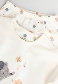 Conjunto de algodón para bebé que incluye una camiseta blanca con gráficos de animales y un pantalón con patrón en colores suaves: azul, melocotón y puntos grises.