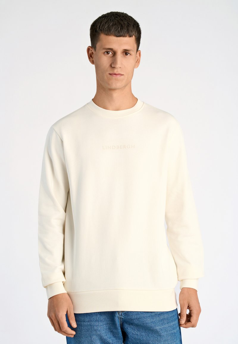 Vit crewneck sweatshirt med subtilt präglad "LINDBERGH"-logotyp, tillverkad av mjukt tyg. Bärs med jeans i blått för en avslappnad look.